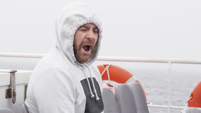 Man wearing a hoody and yawning on a boat