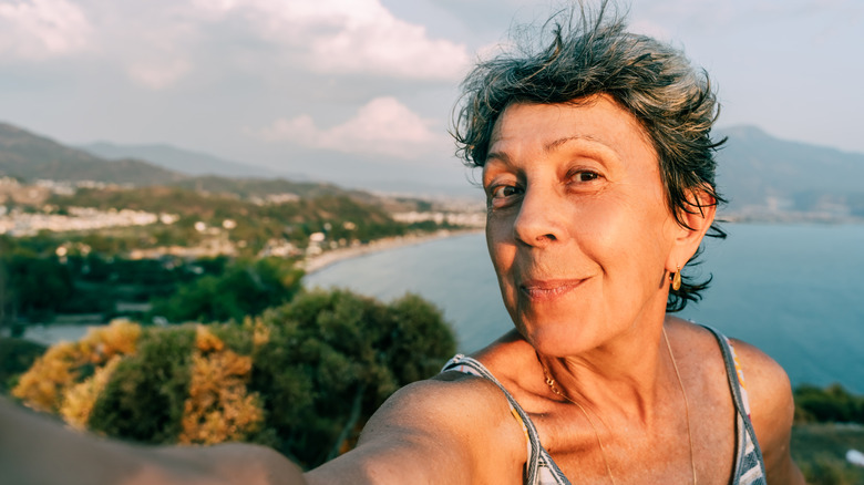Older woman takes selfie at the beach with the sea in the background.