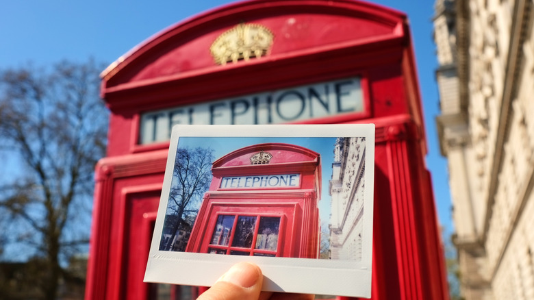 Person takes an instant film photo of a red telephone booth and holds it in front of it.