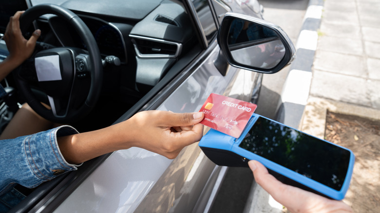 A woman sitting in a rental car makes a contactless payment with a credit card