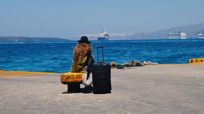 A female tourist sits on a bench next to the water while waiting for a ferry in Greece