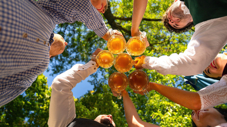 A below shot of a group of friends clinking their glasses under the trees at a German beer garden