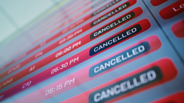 A close up of a departure schedule board with several cancelled flights