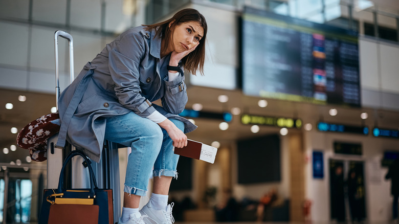 A frustrated woman sitting on her suitcase in the airport