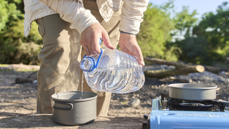 Person pouring water from a jug into a cooking pot while camping