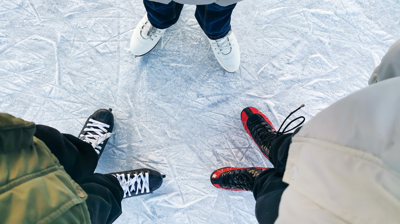 Top-down view of three people's feet in ice skates.
