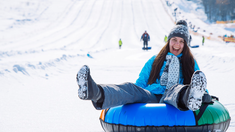 A woman smiling and snow tubing.