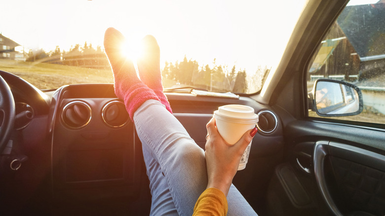 Woman lounging in car, holding cup