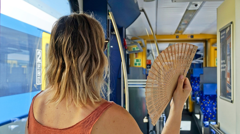 Woman standing on a train during a summer heatwave, cooling herself with a hand fan