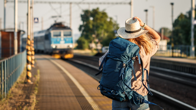 Woman with backpack and straw hat standing at railroad station