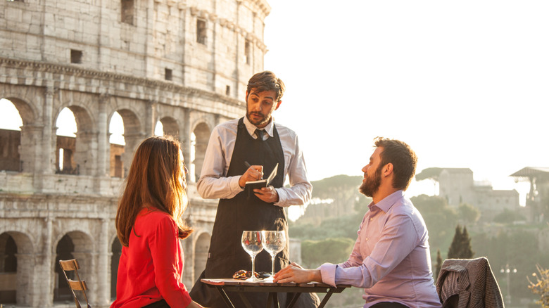 couple ordering food from server at restaurant next to Colosseum in Rome