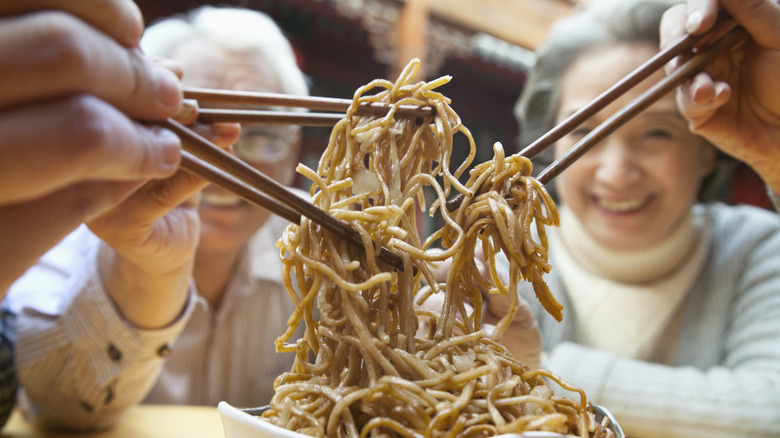 Close-up of three people's hands using chopsticks to pick up noodles.