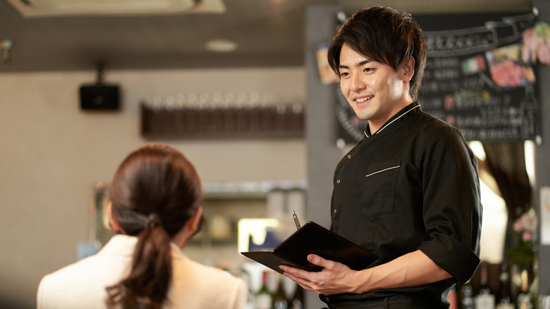 An Asian man taking an order at a restaurant.