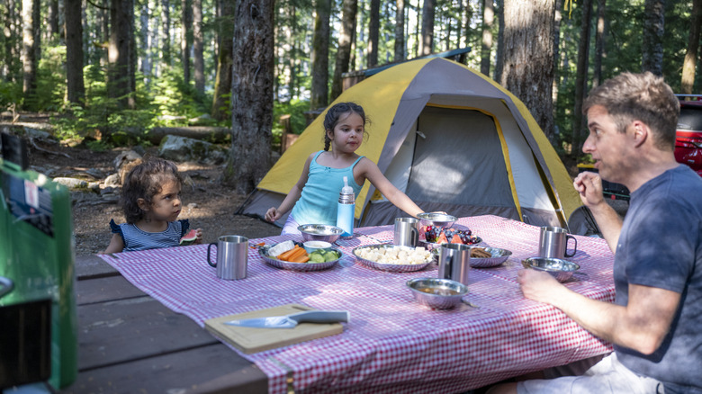 Family eating at a picnic table at campsite in forest