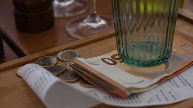 Paper money, coins, and a paper receipt underneath an empty glass.