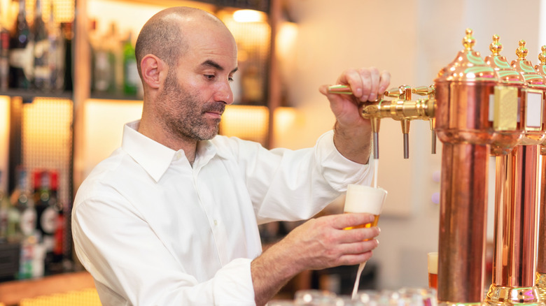 A bartender pouring beer while standing at the bar counter.