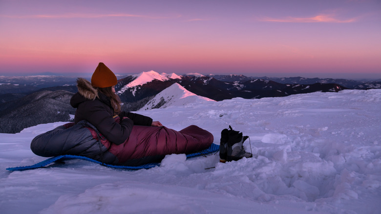 female hiker within sleeping bag at sunset snowy ground