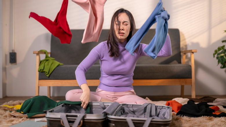 A frustrated woman with nothing to wear throwing clothes in the air.