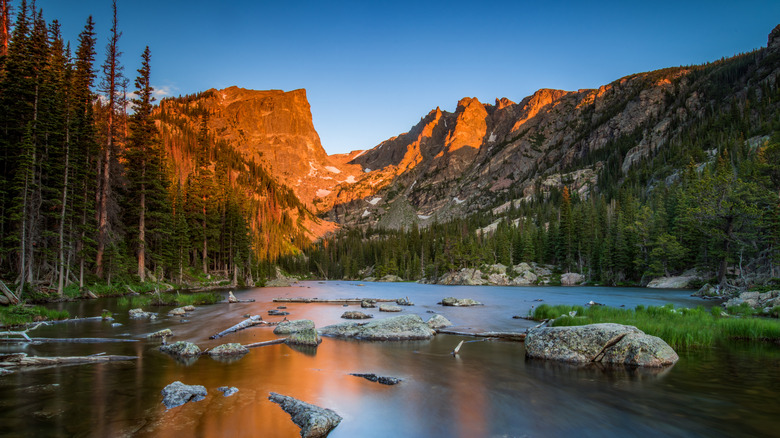 Sun hitting mountain peaks with lake and forest in the foreground in Rocky Mountains National Park