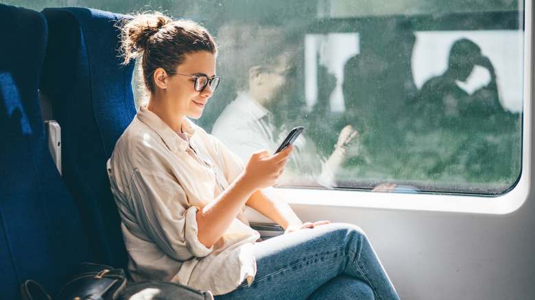 Young woman traveling by train and using phone.