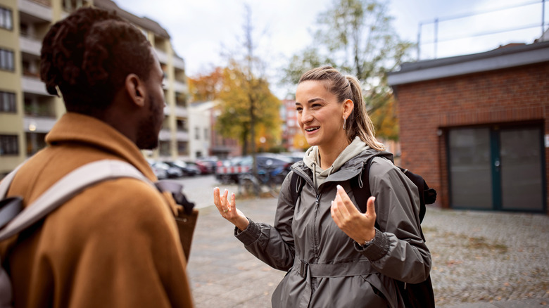 a young woman uses hand gestures while communicating to a man in a foreign language