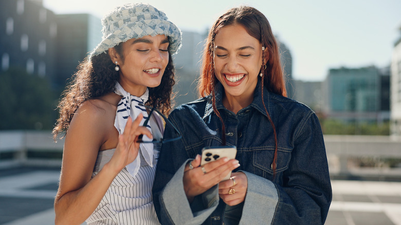 Two women outside watching a video on a phone.