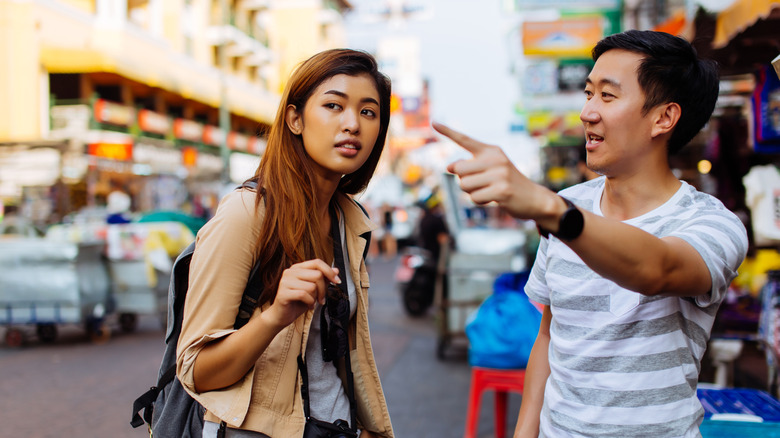 A man points and gives directions to a woman traveler.