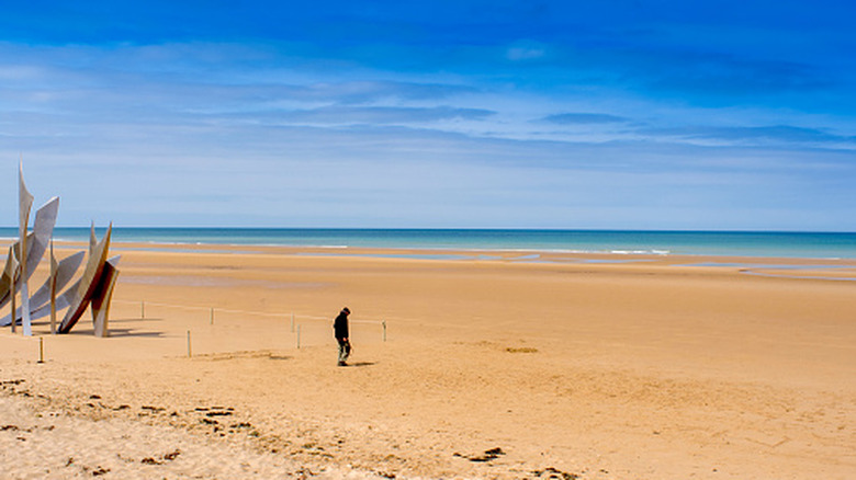 A visitor walks past a monument on Omaha beach sands