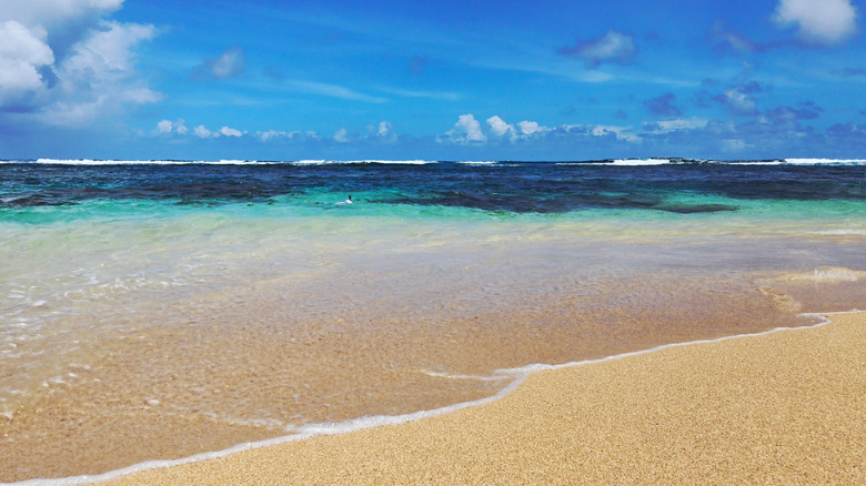 Golden sand beach in foreground with turqouise sea darkening to a deep blue in the background