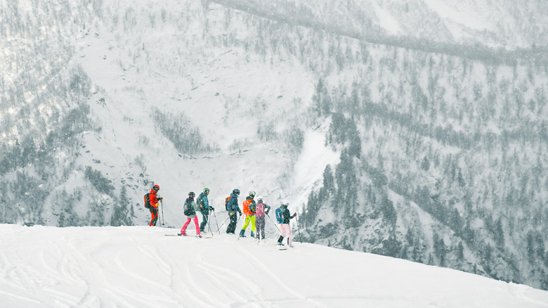 Group of skiers at the top of hill looking at mountain