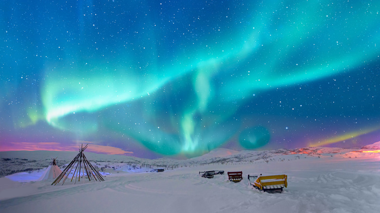 Aurora borealis (Northern lights) in the sky and many wooden snow sleds