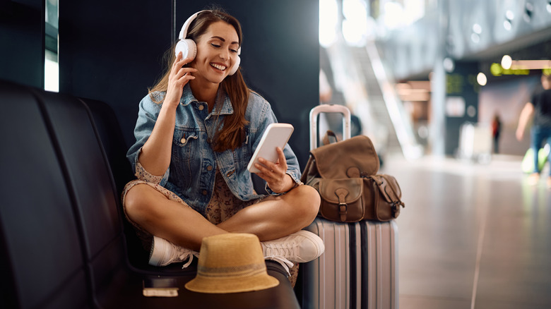 A woman listens to music while checking her smart phone in an airport