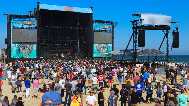 A lively beach crowd by a festival stage