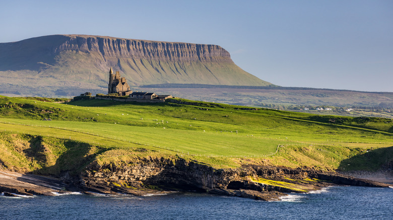 Green fields leading to the sea with a backdrop of a castle and tabletop mountain