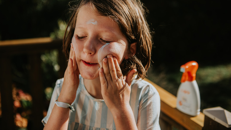 Child applying sunscreen on their face