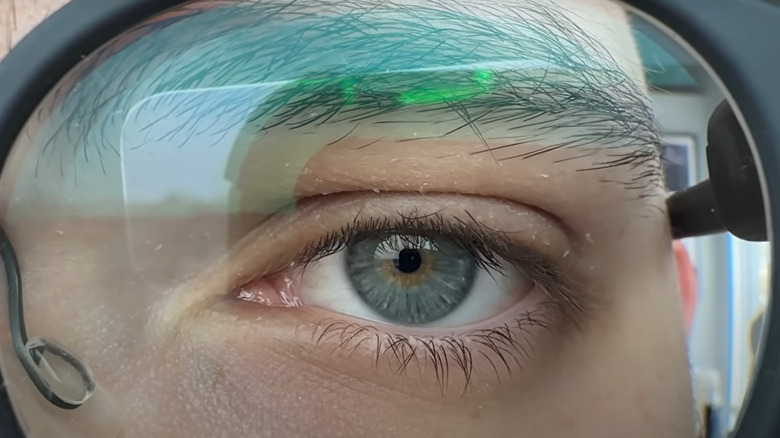 A man's blue eye looking through a glass lens