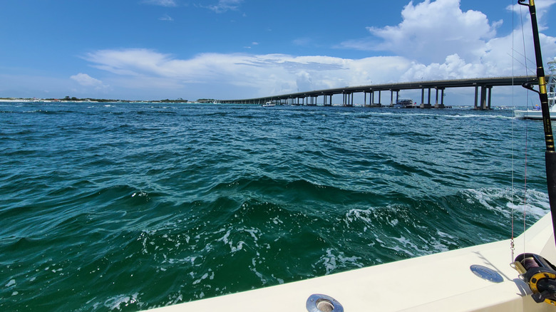 edge of boat with fishing pole, blue ocean, bridge