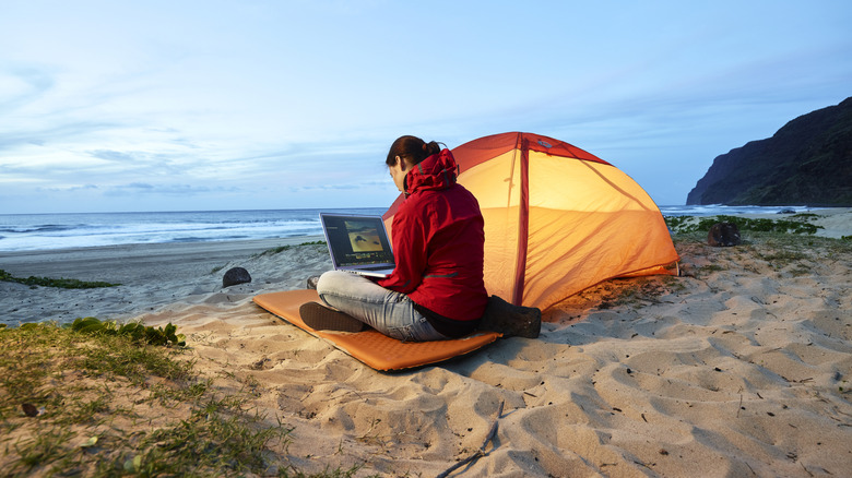 A lady sitting near a tent with a laptop