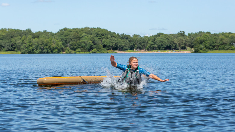 Teenage girl jumping off her paddleboard into the lake
