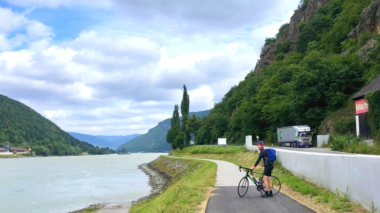 River with mountains in the background and a man posing with a bike