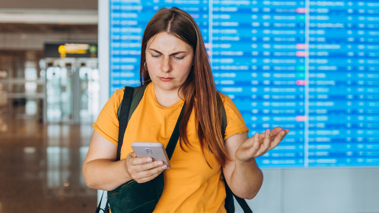 a confused woman at the airport looking at her phone