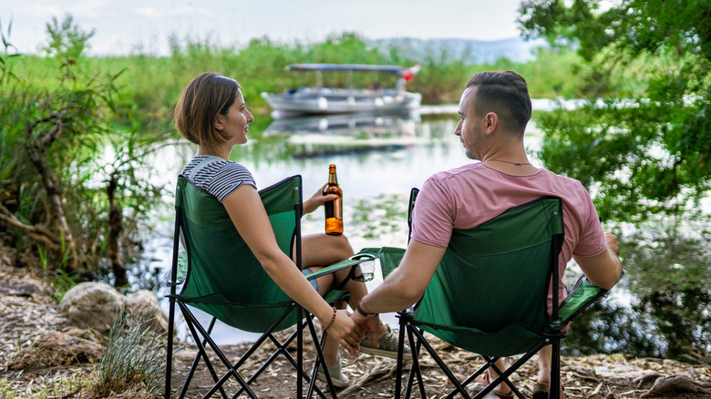 Young couple sitting by the river with camping chairs