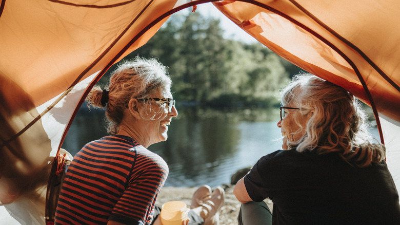 two senior women smiling in a tent by a lake