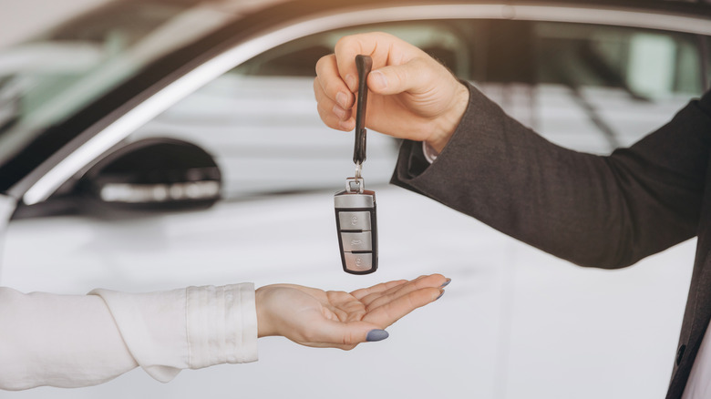 A hand drops a car key into another hand