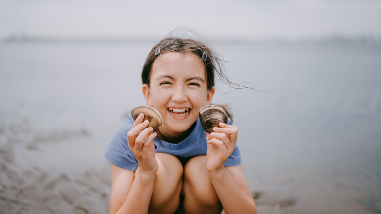 Happy young girl showing clams that she harvested on beach