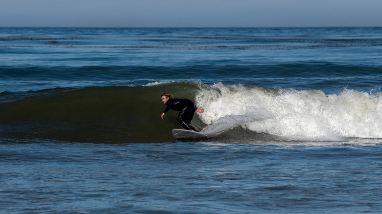 A surfer in black riding an ocean wave at Jalama Beach.