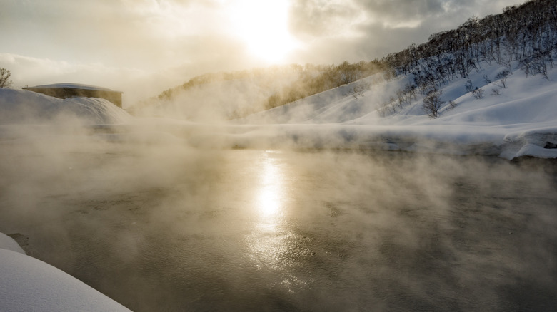Steam off a natural hot spring in Japan with snow in the background