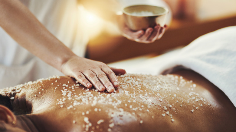 Massage therapist applying a salt scrub on a spa guest