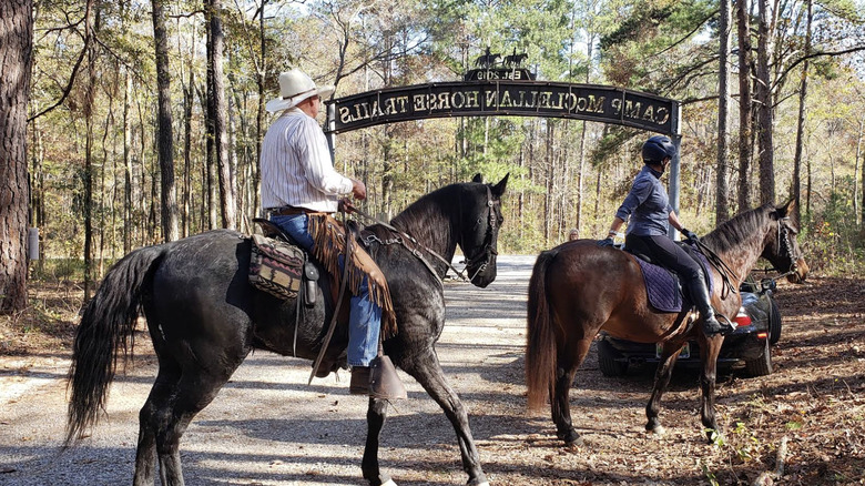 People riding horses in front of a Camp McClellan Horse Trails sign