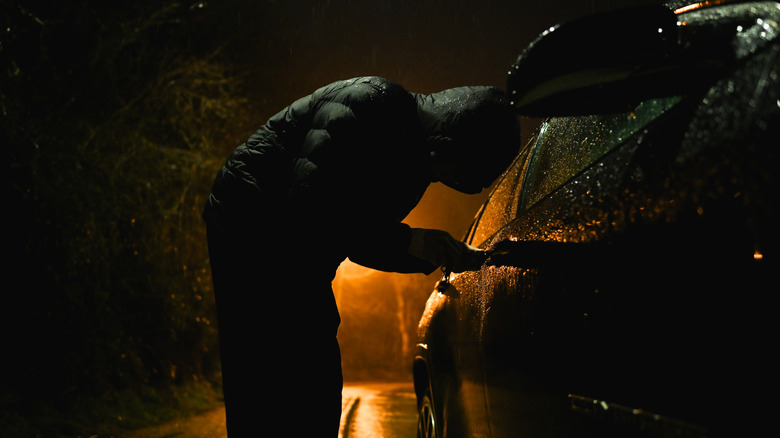 A man with a hood trying to break into a car.